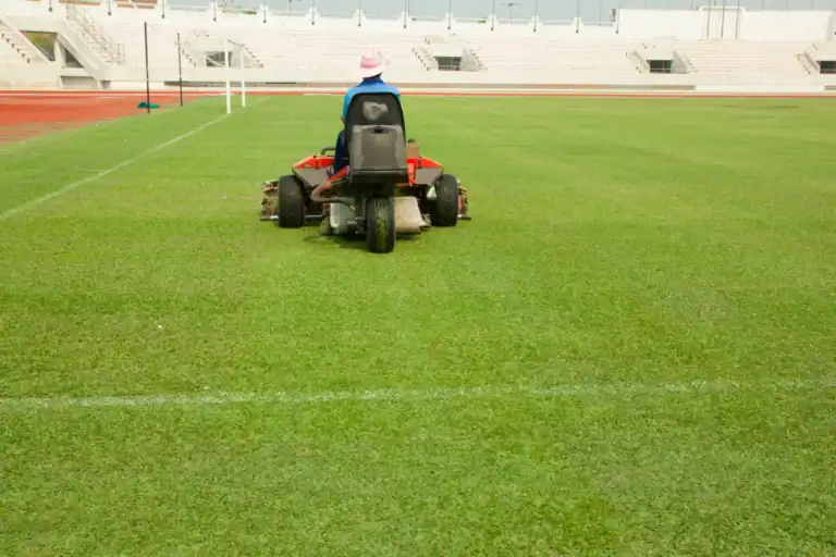 Person riding a lawn mower on a sports field for maintenance.